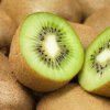 A kiwi cut in half on top of a pile of whole kiwifruit.