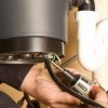 Man's hands holding a power screwdriver to a garbage disposal.