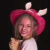 Girl wearing a pig costume with a pink straw hat.