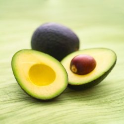 Two avocados, one cut in half with the seed inside.