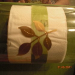 Plastic bottle toilet paper holder hung sideways with leaf design embossed on it.