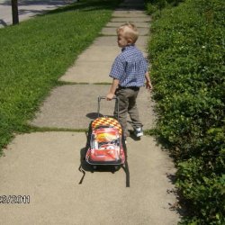 Small boy pulling a loaded sledge or similar wheeless conveyance down the sidewalk. 