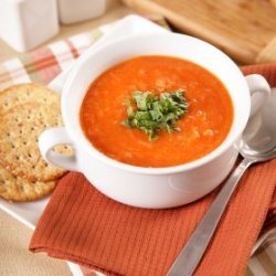 A bowl of tomato soup with crackers.