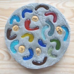 A homemade stepping stone with glass pieces and rocks placed in the cement.