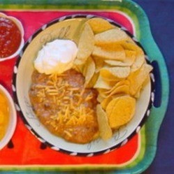 Serving tray with pasta bowl of bean dip, chips, sour cream, and a side of salsa. 