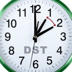 Close up of image of a white clock face with green border. The clock has DST written on it and two hour hands exactly one hour apart with a red double ended arrow pointing at both hands indicating the hour changes forward and back by one hour