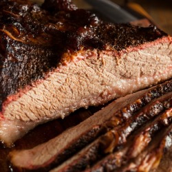 Close up of beef brisket partially sliced on a wooden cutting board