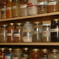 Wide variety of different types and sized of jars filled with spices on three shelves all with different types of labels