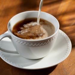 Liquid creamer being poured into white coffee cup on a table