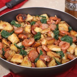 Skillet containing fried sausage and potatoes with onions and greens