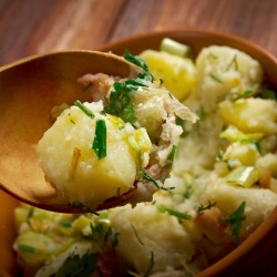 Spoon holding german potato salad over a bowl of same.