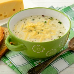 Bowl of cheesy potato soup with shredded cheese on top in green bowl on a green plaid napkin