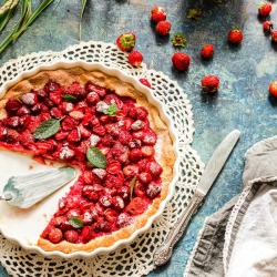 Strawberry Pie with several pieces missing surrounded by ripe strawberries
