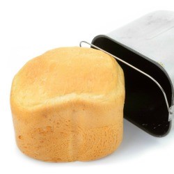White loaf of bread machine bread laying next to a bread machine pan
