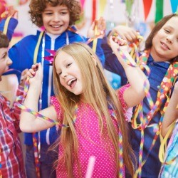 10 year old girl surrounded by friends with streamers, party blowers, and party hats 