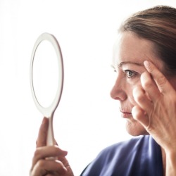A woman looking at her face in a mirror.