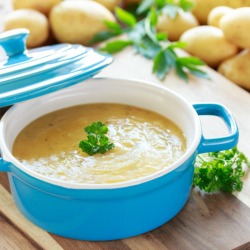 Bowl of potato soups surrounded by potatoes
