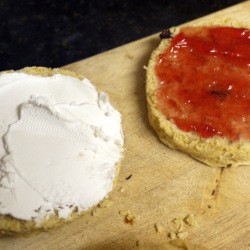A scone with cream on one side and jelly on the other.