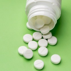 An aspirin bottle on it's size with aspirin pills spilling out of it.