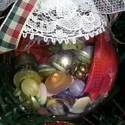Clear plastic ornament filled with buttons and decorated with lace, netting, and ribbon hanging on the tree.