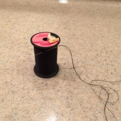 Pre-thread Your Needles - spool of black thread with a rethreaded needle stuck in the thread