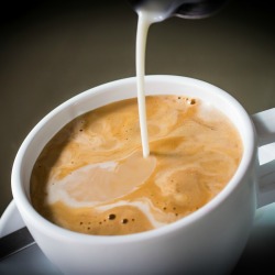 Pouring liquid coffee creamer into a cup of coffee.