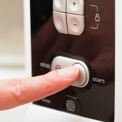 A finger pushing a start button on a microwave.