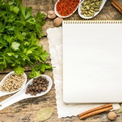 A notebook with spices on a wooden cutting board.