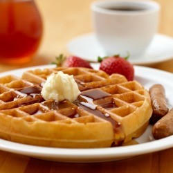 A plate of waffles with syrup and butter.