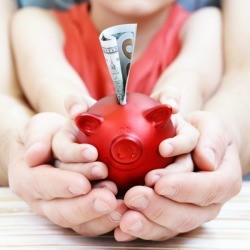 A red piggy bank being held by a child's hands and then an adult's hands.