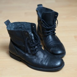 A pair of boots with black rubber soles on a wood floor.