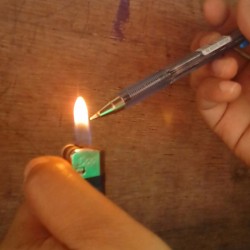 A ballpoint pen being heated in the flame of a pocket lighter.