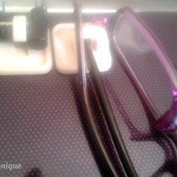 Cords and eyeglasses hanging on Command hooks on the side of a laptop.