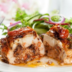 A stuffed chicken breast on a plate with salad.