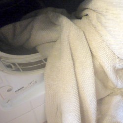 A white towel being placed in an open dryer.