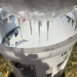 Allowing paint to drip from the strainer into a plastic container.