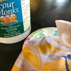 A bottle of vinegar and a white cleaning pad over a shirt with a sticker mark.