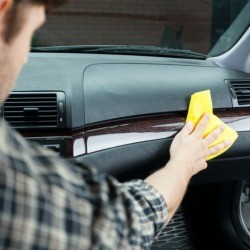 A man cleaning his car's dashboard to remove smoke odors.