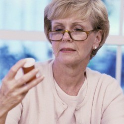 An woman wearing glasses reading a bottle.