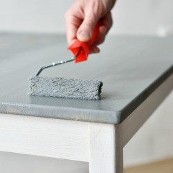 A painting a wood table using a roller.