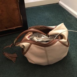 A phone inside a handbag with a phone attached to a power cord in the wall.