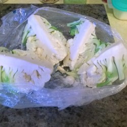 A bag that contains a head of cauliflower from the grocery store, cut in quarters