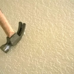 A hammer claw being used upside down to remove a nail from the wall.