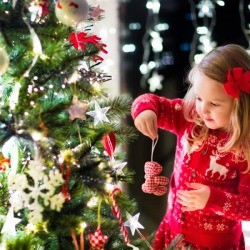 Child in red knitted Nordic reindeer sweater decorating Christmas tree