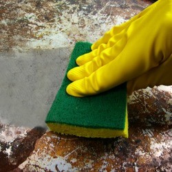 Rubber glove cleaning a burnt pan with a sponge.