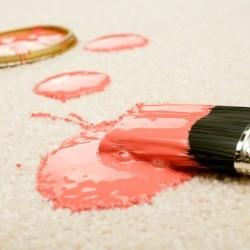 Paint brush, paint can lid and blobs of pink paint on a light carpet.
