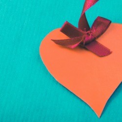 Orange paper heart with a red ribbon, on a aqua colored cardstock.