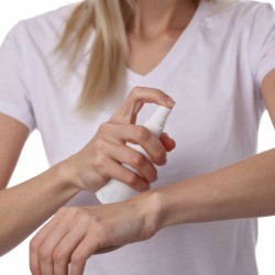 Woman spraying her arm with insect repellent.