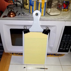 A small legal pad attached to a small cutting board with binder clips. 
