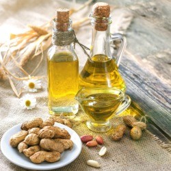 Peanut oil in 2 glass bottles with a plate of peanuts.